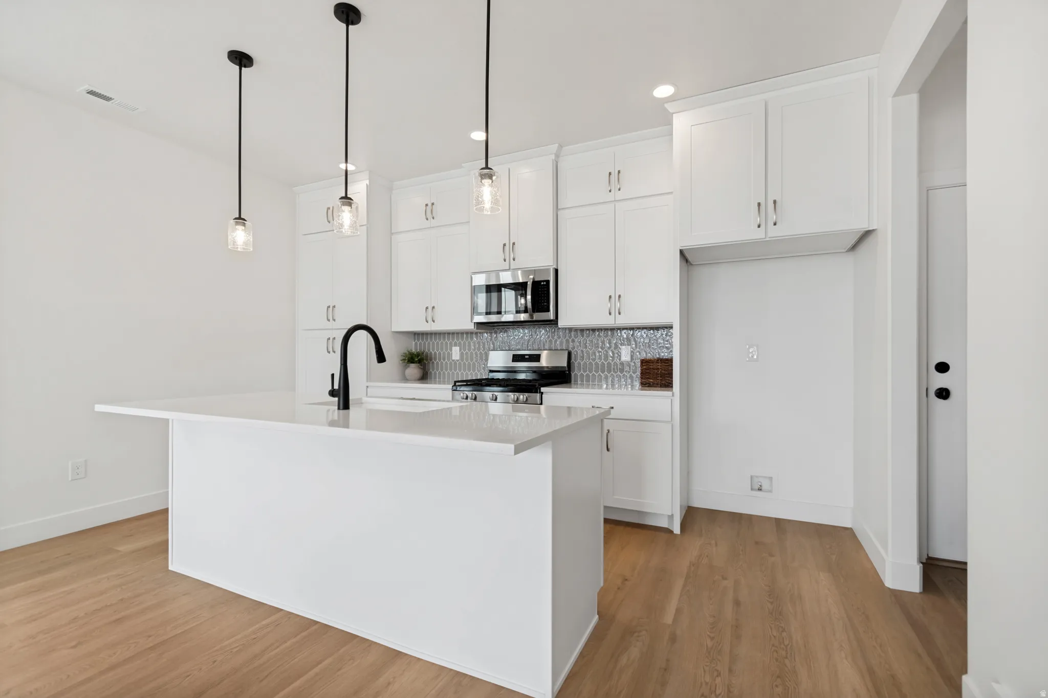 Kitchen featuring a large island with sink, white shaker-style cabinetry, stainless steel appliances, and wood-finish flooring