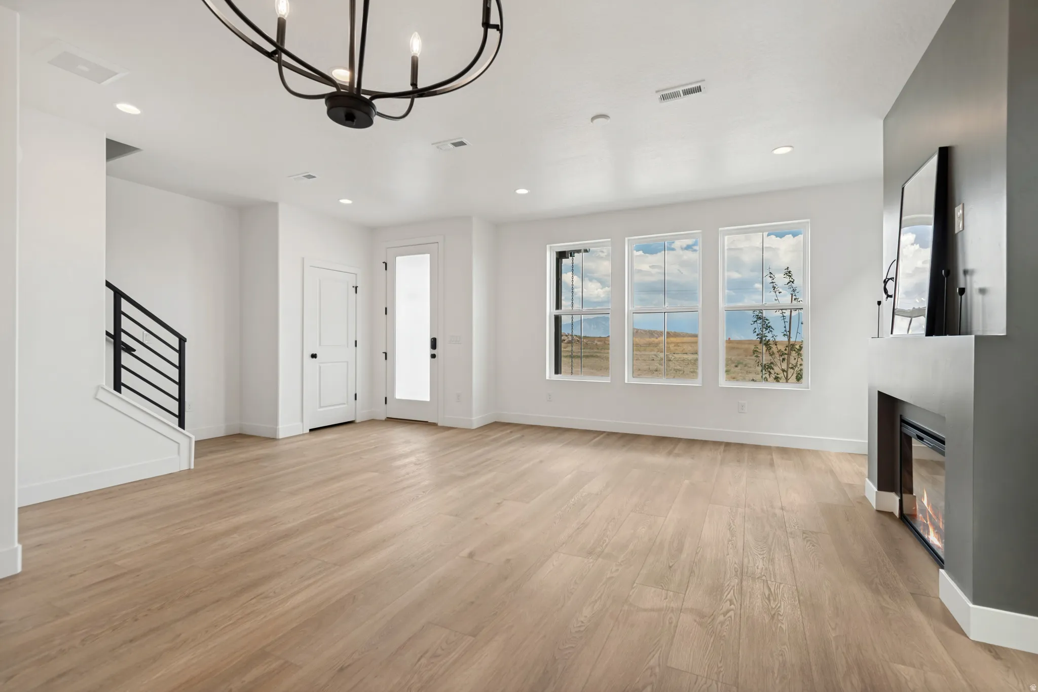 Recessed lighting, wood-finish flooring, staircase with metal railing, contemporary fireplace, and multiple windows