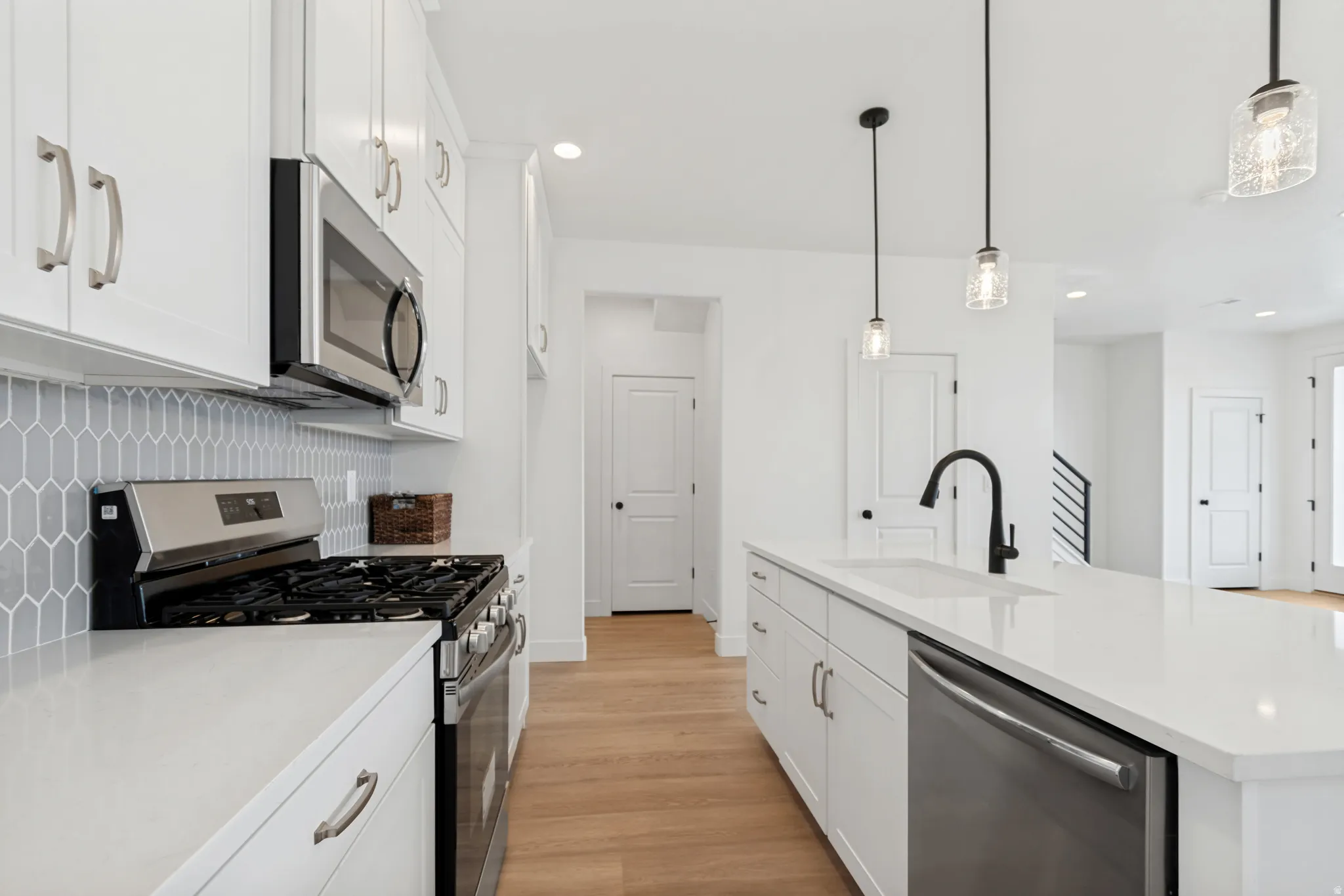 White cabinetry, light wood-finish flooring, stainless steel appliances, white countertops, and a gray geometric tile backsplash