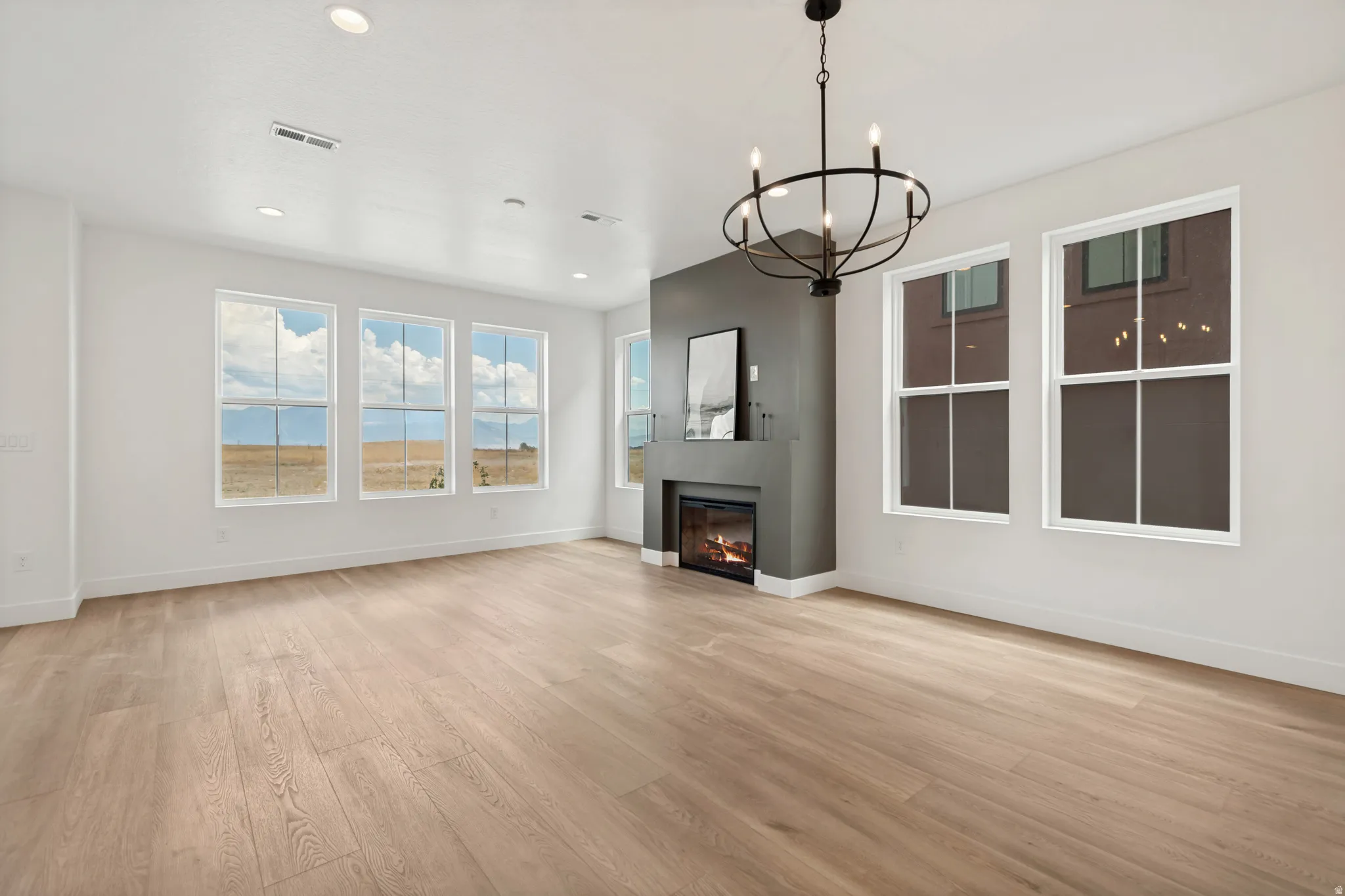 Spacious room featuring light wood-finish flooring, a contemporary fireplace with a dark gray surround, and multiple large windows
