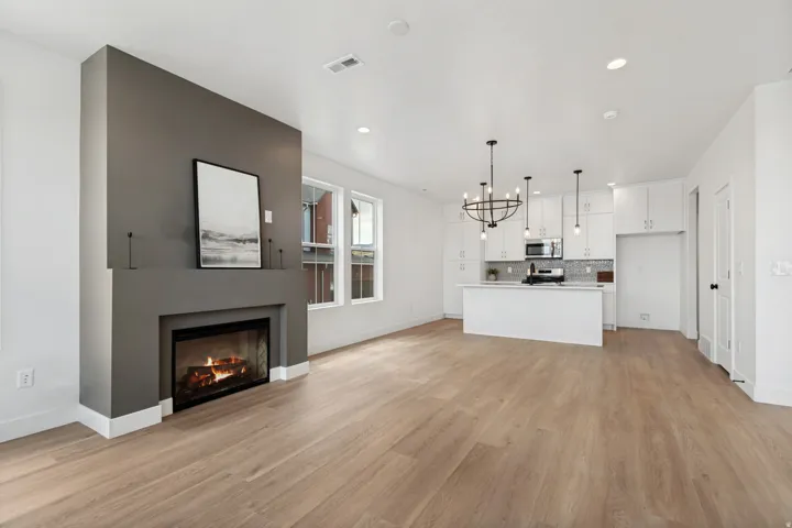Open-concept living space with wood-finish flooring, a contemporary fireplace, and a kitchen featuring white cabinetry, an island, and pendant lighting