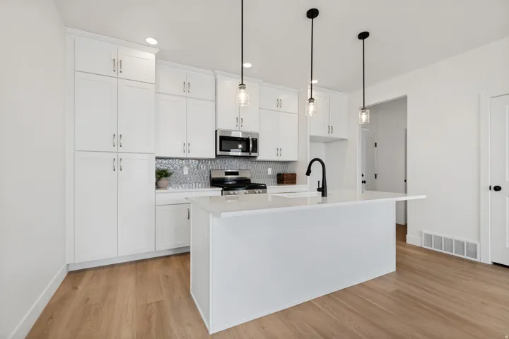 White cabinetry, wood-finish flooring, white kitchen island with counter, stainless steel appliances, and pendant lighting