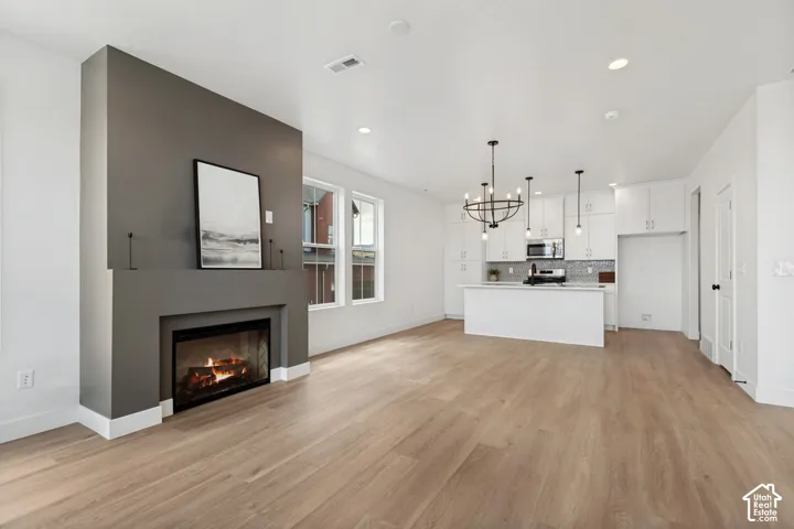 Open-concept living space with wood-finish flooring, a contemporary fireplace, and a kitchen featuring white cabinetry, an island, and pendant lighting