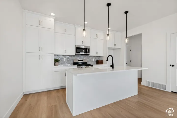 White cabinetry, wood-finish flooring, white kitchen island with counter, stainless steel appliances, and pendant lighting