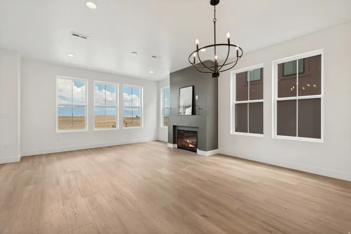 Spacious room featuring light wood-finish flooring, a contemporary fireplace with a dark gray surround, and multiple large windows
