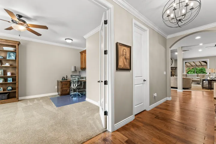 Hardwood-finish flooring, crown molding, arched entryways, and a ceiling fan with integrated lighting