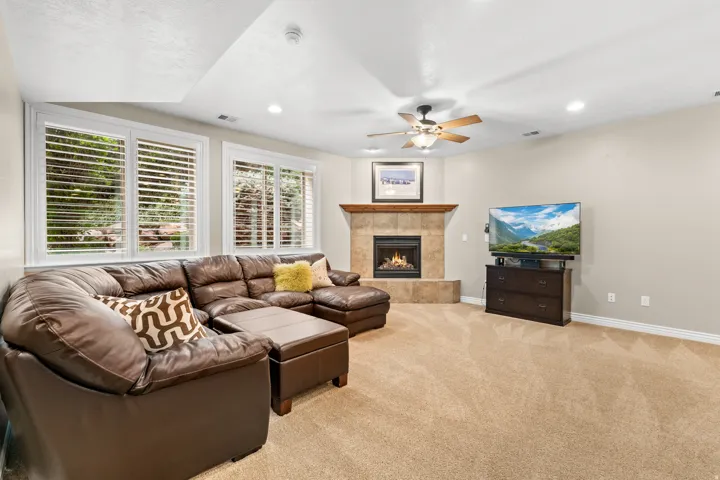 Spacious living area featuring a corner fireplace with a tile surround and wood mantle, recessed lighting, ceiling fan, and carpet flooring