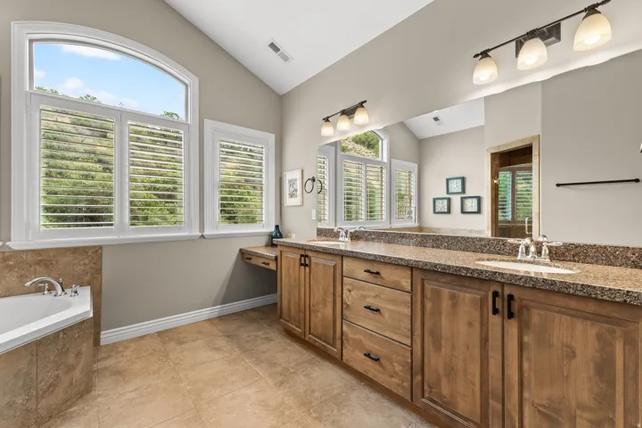 Dual vanity with solid surface countertops, natural wood-finish cabinetry, and an integrated makeup desk