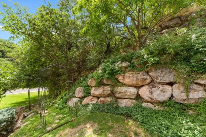 Tiered landscaping featuring natural stone retaining walls, mature trees, and a decorative metal archway