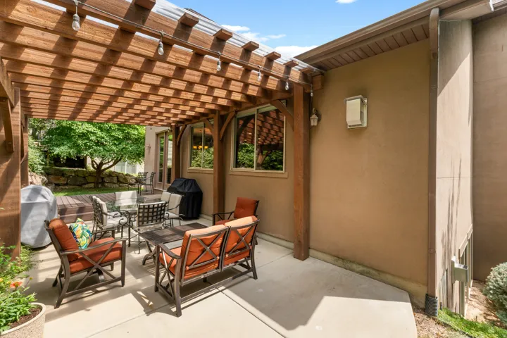 Expansive concrete patio with a wooden pergola, outdoor lighting, and a stucco exterior
