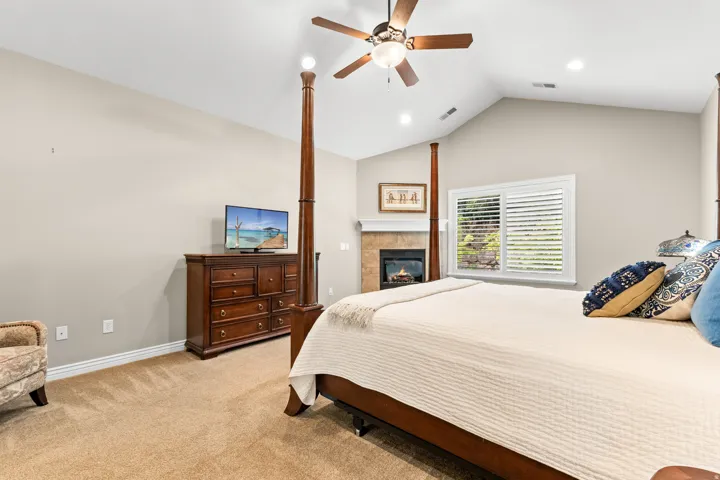 Vaulted ceiling featuring a ceiling fan, fireplace with a stone surround, and plantation shutters on the window
