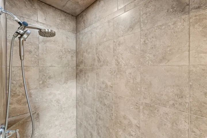 Tiled shower enclosure featuring a fixed showerhead and handheld shower attachment