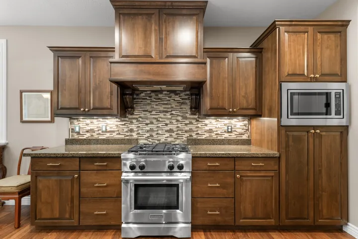 Dark wood-finish cabinetry featuring brushed gold hardware, stone countertops, and a full-height mosaic tile backsplash