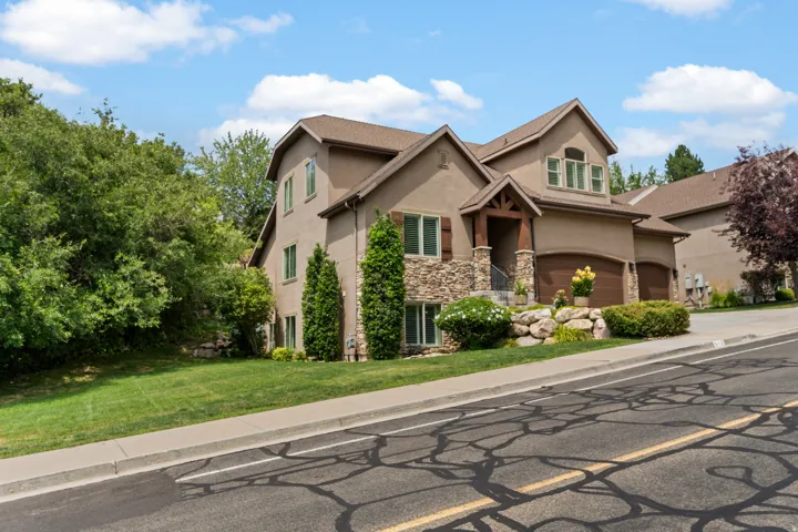 Stucco exterior with stone accents, covered entry, attached multi-car garage, and established landscaping