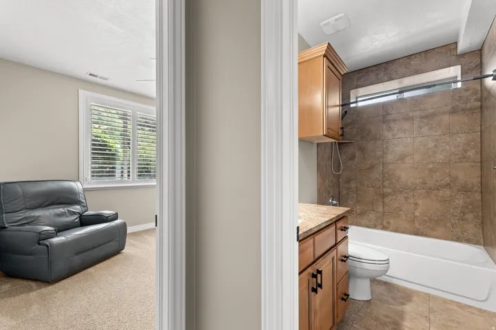 Bathroom featuring a bathtub with a tiled shower surround, a wood-finish vanity with a countertop, and an upper wood-finish cabinet