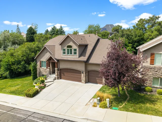 Stucco and stone exterior with architectural shingles, arched garage doors, and a concrete driveway