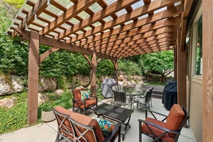Outdoor patio featuring a wood pergola with a translucent roof, a concrete patio surface, a tiered wooden deck, and a natural rock retaining wall