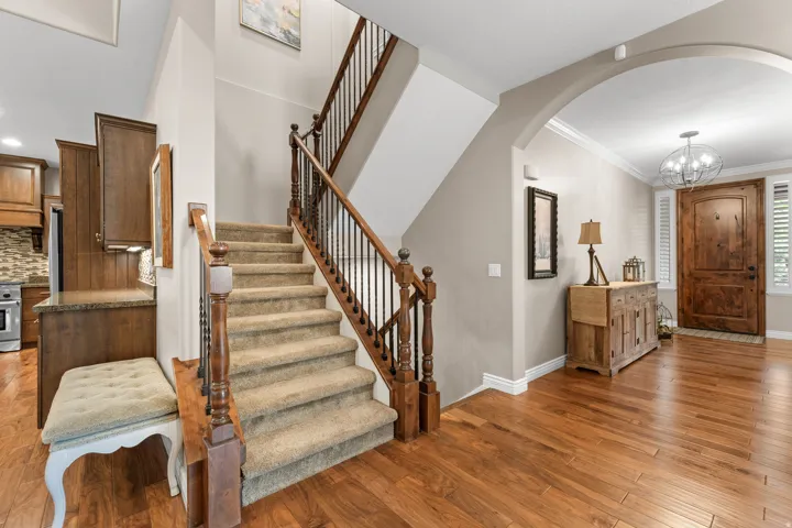 Warm wood-finish flooring, carpeted staircase with wood and iron balusters, arched doorway, wood entry door, and crown molding