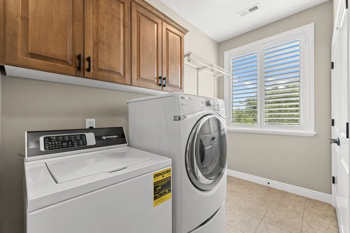 Laundry area featuring wood-finish cabinetry, a window with plantation shutters, tile flooring, and a built-in hanging rack