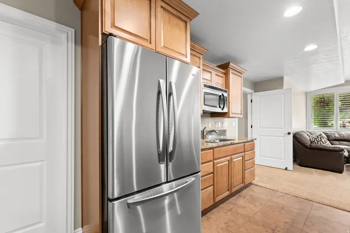 Stainless steel French door refrigerator, wood-finish cabinetry, built-in microwave, granite-style countertop, and tile flooring