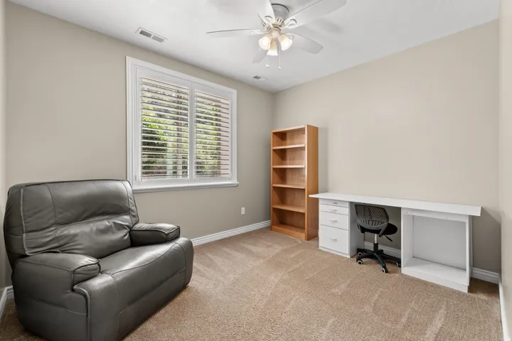 Carpeted room featuring a window with white shutters, a ceiling fan, and painted walls