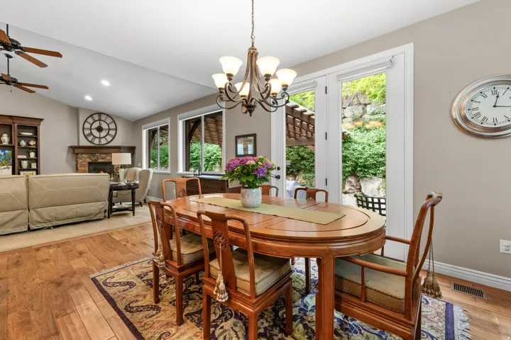Vaulted ceiling with dual ceiling fans, wood-finish flooring, stone-clad fireplace, built-in shelving, and double glass doors opening to outdoor space