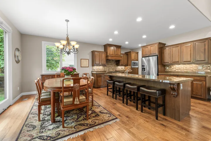Kitchen and dining area featuring wood-finish flooring, wood cabinetry, stainless steel appliances, granite countertops, and recessed lighting