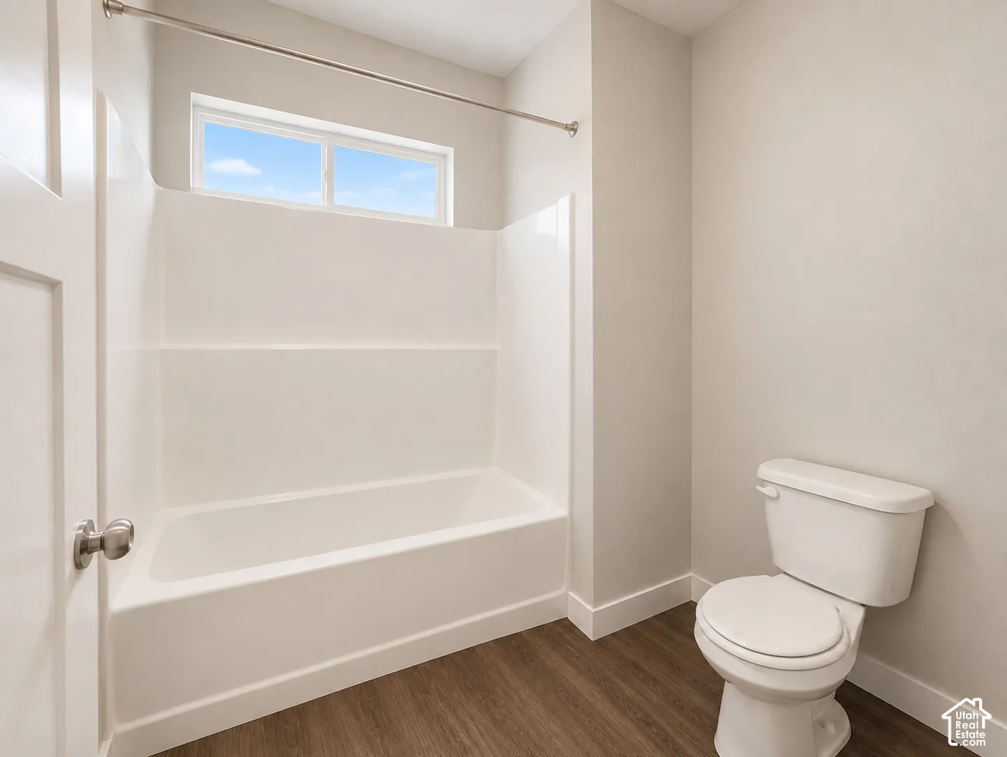 Primary room bathtub and shower combination unit, wood-finish flooring, white toilet, and a window