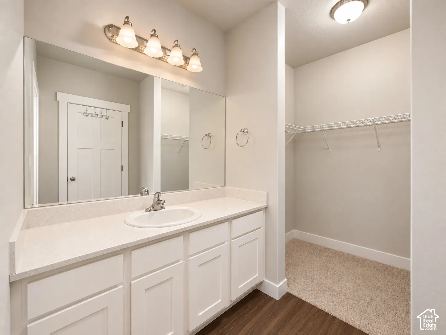 Primary room vanity with an integrated sink and brushed nickel faucet, large mirror, white shaker-style cabinetry, and overhead bar lighting