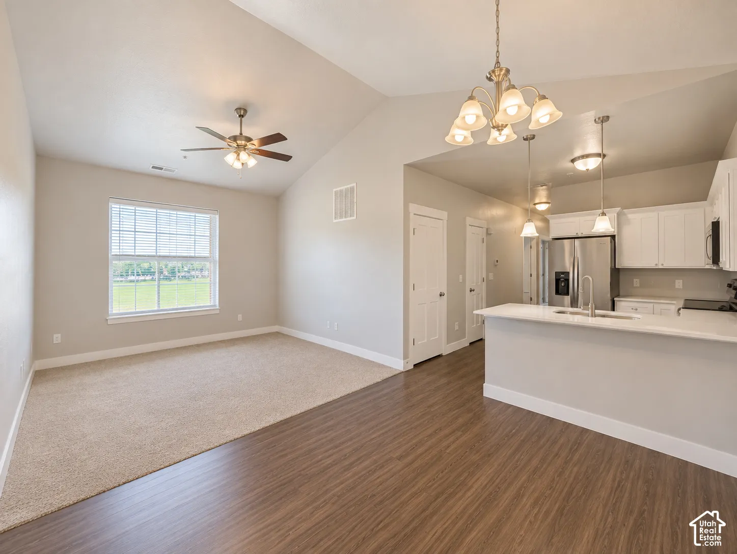 Vaulted ceiling with ceiling fan, white kitchen cabinetry, stainless steel appliances, white countertop, and wood-finish flooring