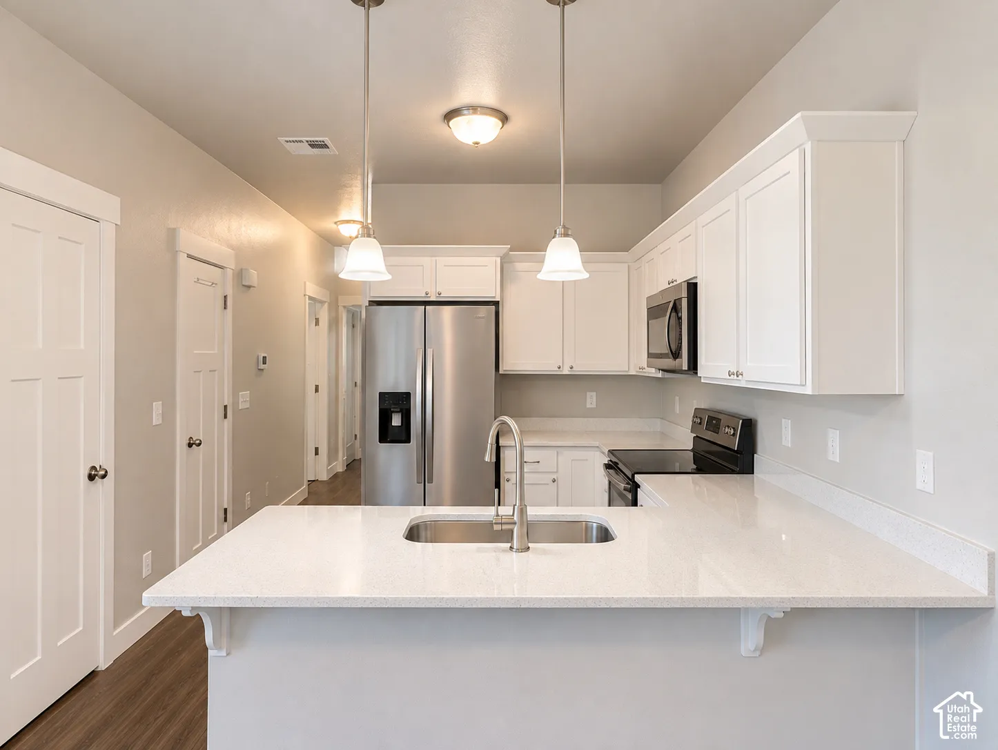 Kitchen featuring white shaker-style cabinetry, stainless steel appliances, a double basin sink, light-toned countertops, and wood-finish flooring