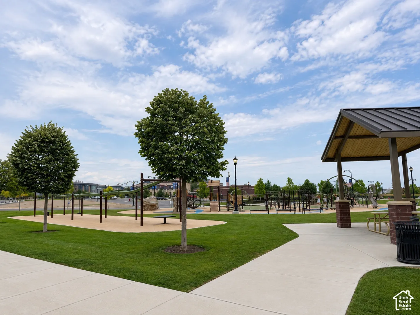 Expansive green space featuring a paved walkway, mature trees, and a covered picnic area