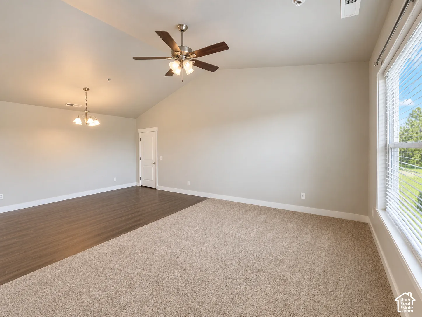 Vaulted ceilings with a ceiling fan, dual-tone flooring, and a large window with horizontal blinds