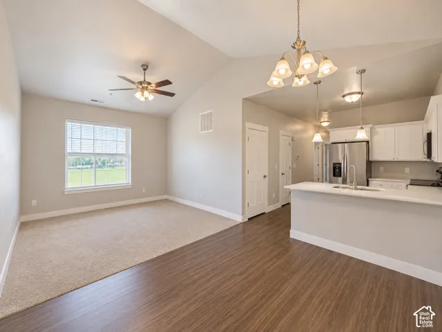 Vaulted ceiling with ceiling fan, white kitchen cabinetry, stainless steel appliances, white countertop, and wood-finish flooring