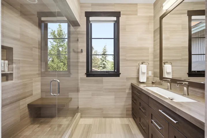 Glass-enclosed shower with a wood-finish bench, dual windows, and a built-in recessed shelf