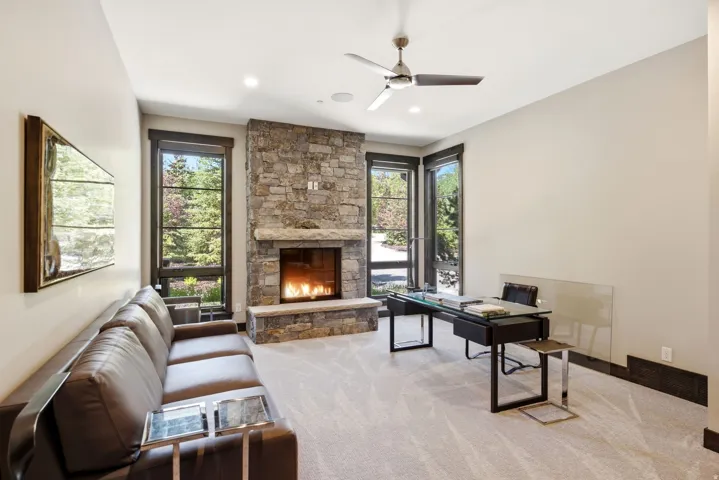 Stone fireplace with a hearth, carpeted flooring, large windows with dark trim, recessed lighting, and a ceiling fan