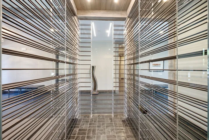 Glass panel walls with horizontal metal accents, gray stone tile flooring, and wood-paneled ceiling