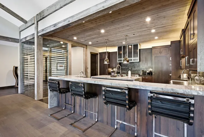 Kitchen island with a light-toned countertop and wood-paneled base, wood-finish flooring, wood-paneled ceiling with recessed lighting, and a glass-enclosed wine storage area