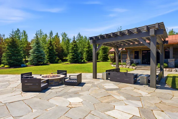 Flagstone patio with a built-in stone fire pit, a wooden pergola, and a manicured lawn