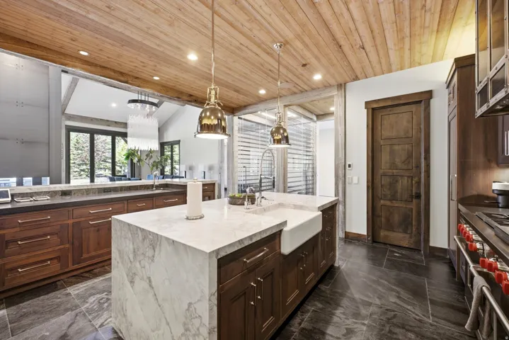 Kitchen featuring a large center island with a farmhouse sink, wood cabinetry, stone countertops, and a wood-paneled ceiling