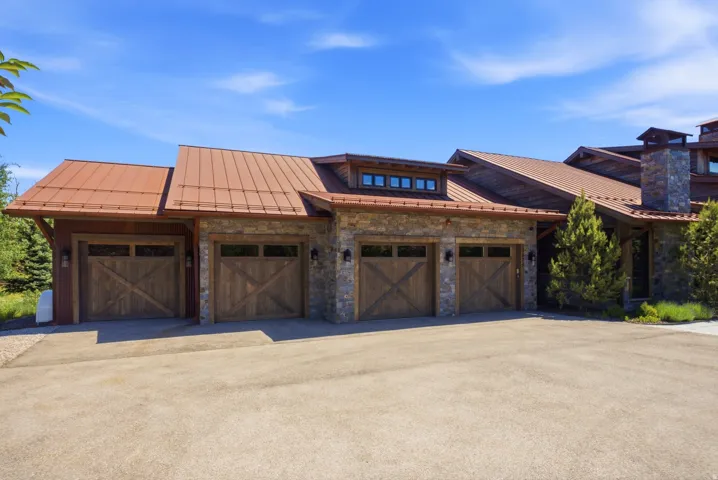 Three-car garage with wood-finish doors, stone facade, copper-tone metal roofing, and dormer windows