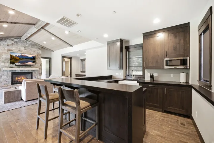 Stone-clad fireplace, vaulted ceiling with wood-finish planks, wood-finish flooring, dark wood cabinetry, and a built-in microwave
