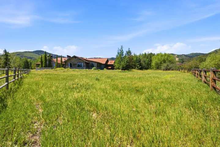 Expansive grassy field with a wooden split-rail fence and distant mountain backdrop