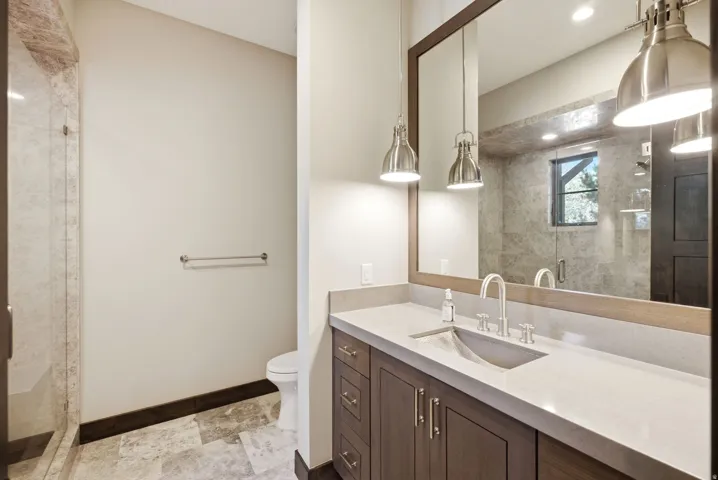 Walk-in shower with glass enclosure, custom vanity with integrated sink, rectangular framed mirror, and brushed nickel pendant lighting