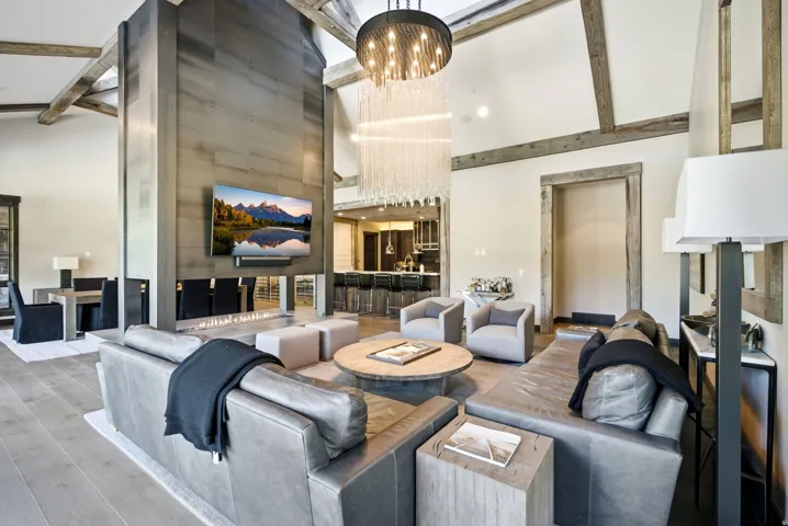 Vaulted ceilings with exposed beams, a floor-to-ceiling fireplace with integrated television, wood-finish flooring, and a contemporary chandelier