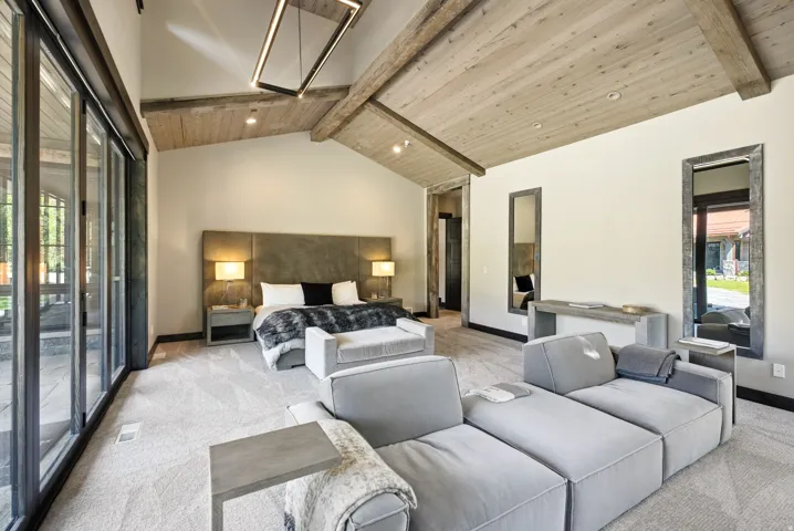 Vaulted wood plank ceiling with exposed beams, large format sliding glass doors, contemporary linear chandelier, and built-in mirror accents