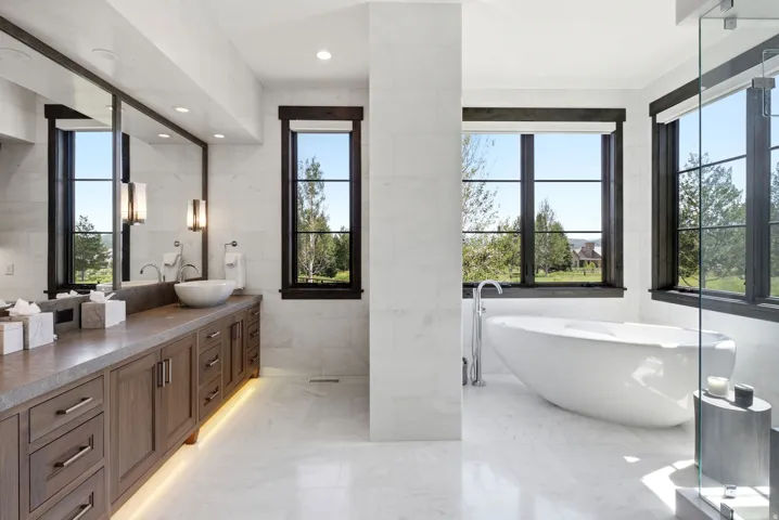 Dual vessel sinks, expansive vanity with extensive storage, freestanding soaking tub, and large windows with dark trim