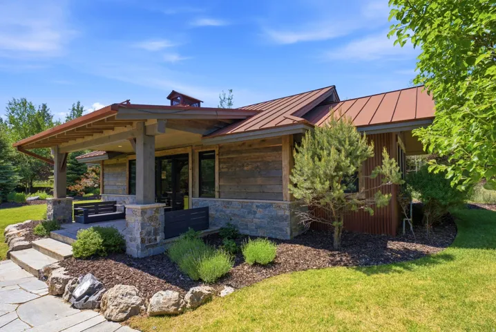 Exterior featuring stone and wood siding, a standing seam metal roof, covered patio with wood beams, and a natural stone pathway