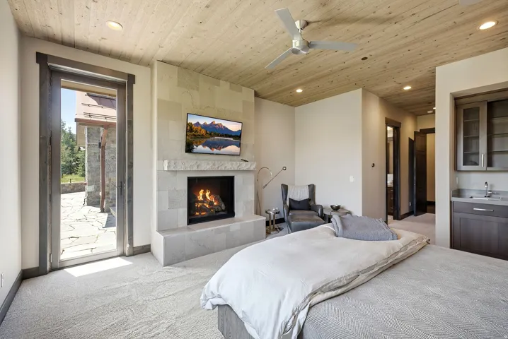 Stone-clad fireplace with mantel, wood-plank ceiling, recessed lighting, ceiling fan, and built-in wet bar with cabinetry