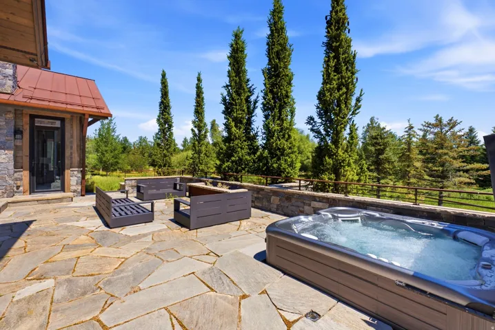 Expansive stone patio featuring a built-in spa, stonework retaining wall, and mature evergreen trees